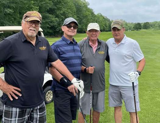 Four men standing on a golf course and smiling at the camera