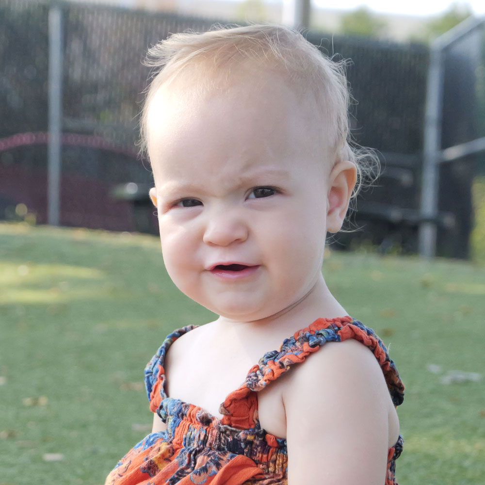Child sitting outside on the graph smiling for a photo.