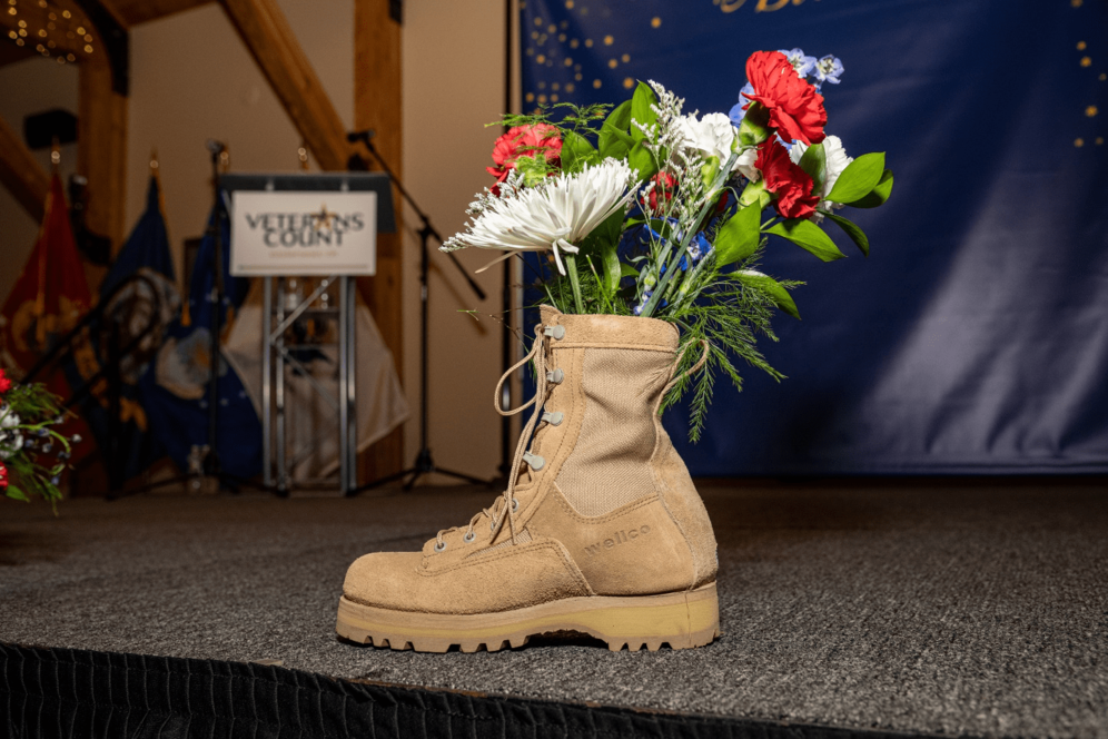 a single boot is placed on a stage, with a bouquet of flowers sticking out the top