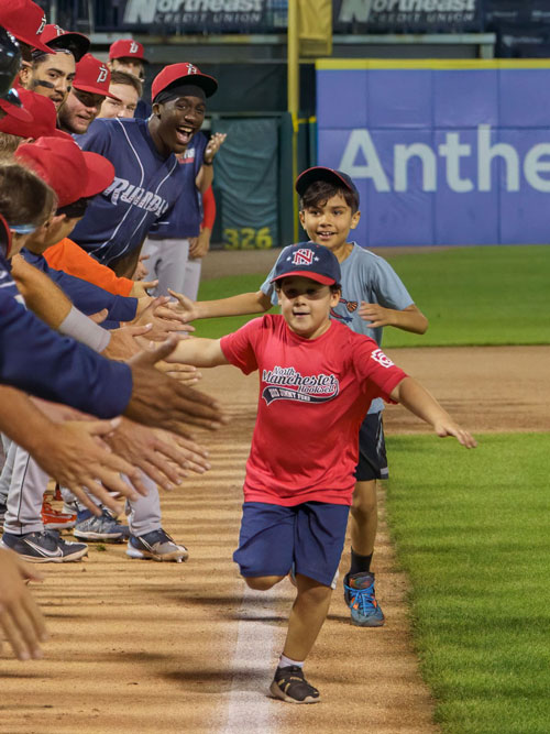 Two children running down the baseline at the Fisher Cats game giving Hi-Fives to the players.