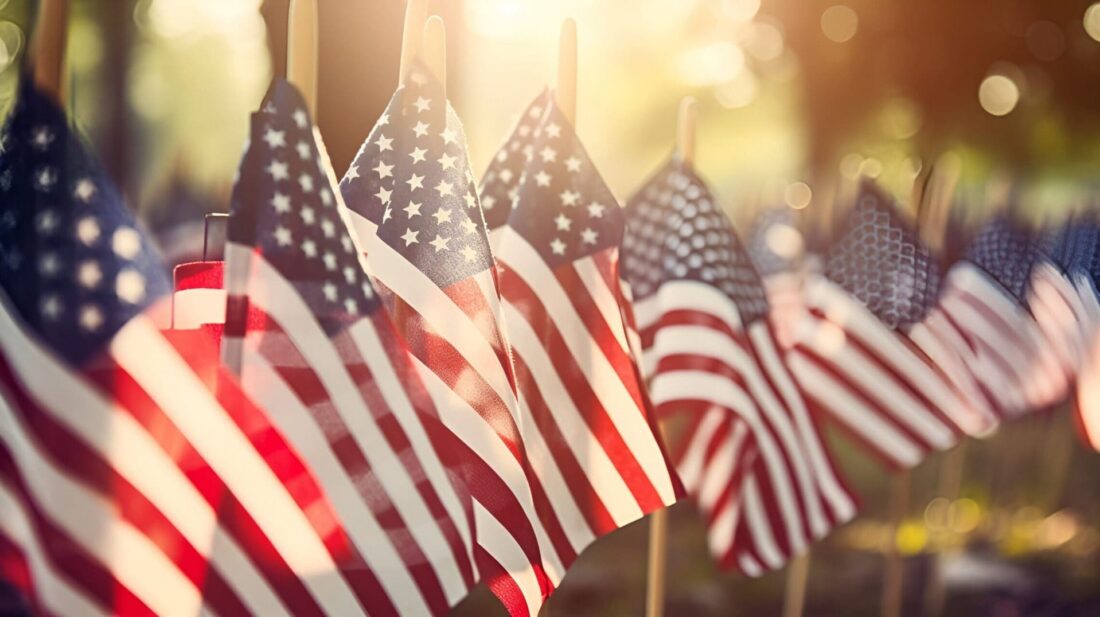A row of flags standing in Remembrance on Memorial Day in the Unit amidst sunlight and big trees