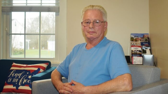 Man in light blue t-shirt sittings in a gray chair.