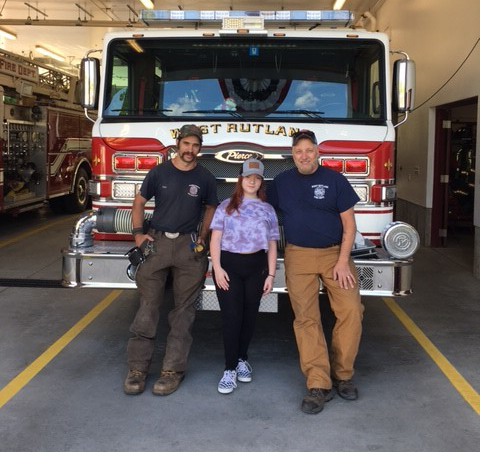 novalee stands in front of a firetruck with two firefighters